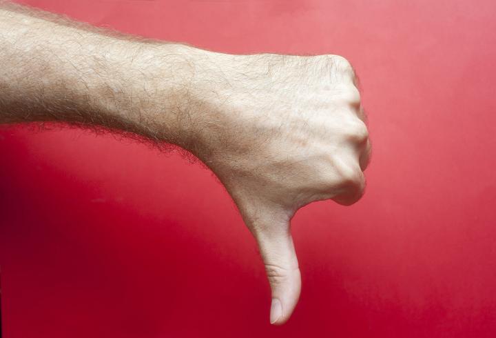 Man making a thumbs down gesture over a red background signalling his disapproval and failure