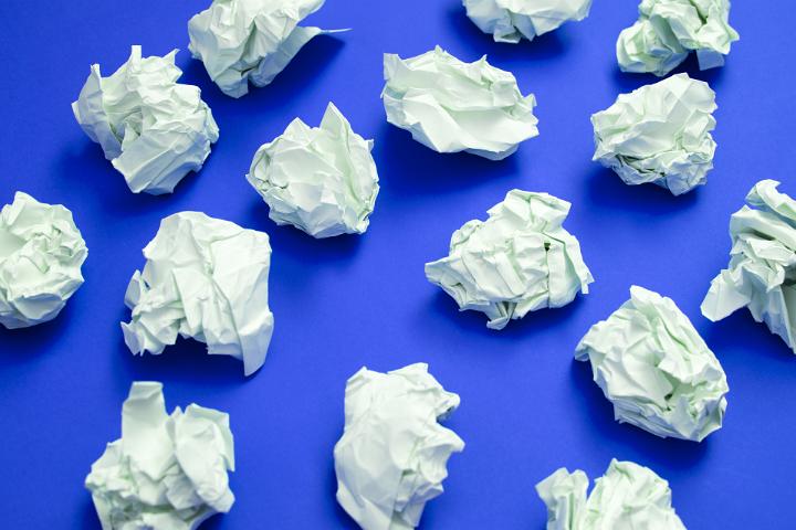 Writers block concept or business impasse with scattered balls of crumpled white paper with discarded ideas on a blue background viewed from above