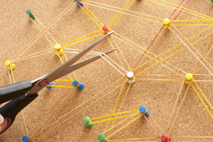 Scissors Cutting Elastic Bands Connected by Thumb Tacks Inserted into Cork Board in Business Networking Communication Concept Image