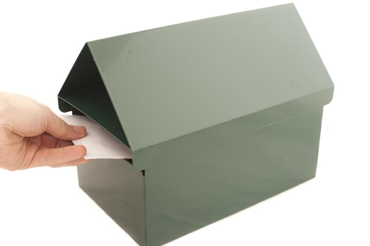 Postman delivering mail placing a letter into a metal letterbox, closeup of his hand isolated on white