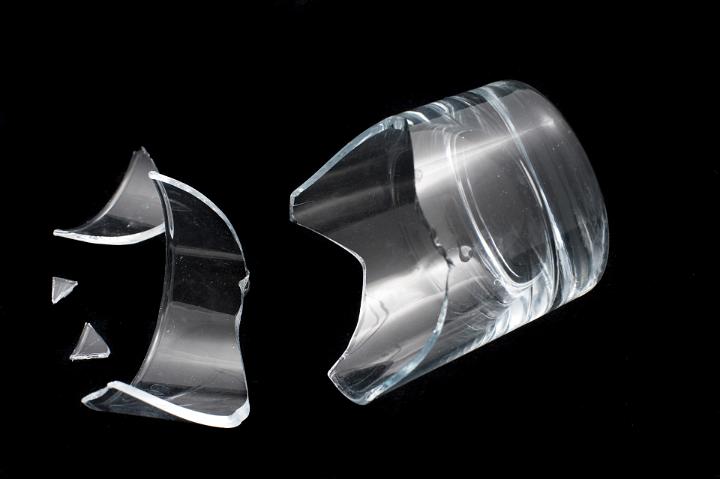 Broken glass tumbler lying on a black background with remnants and sharp shards following an accidental drop