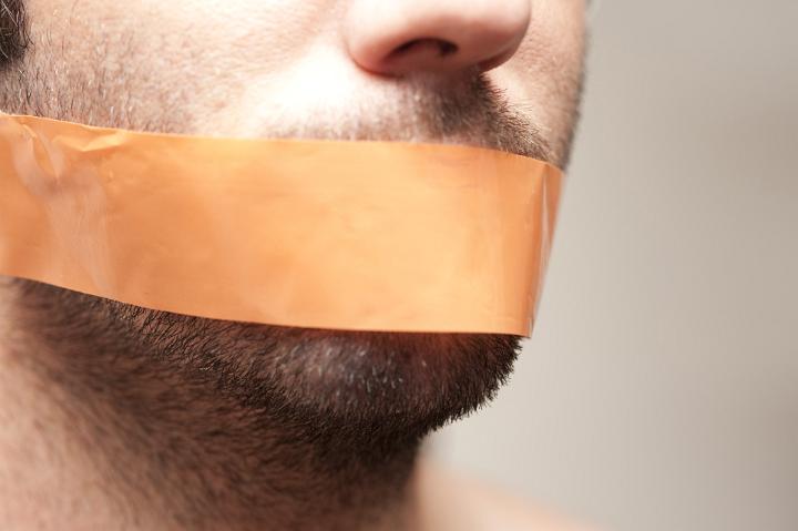 Can't Speak - Close Up of Man with Facial Hair Stubble Gagged with Orange Tape Across Mouth