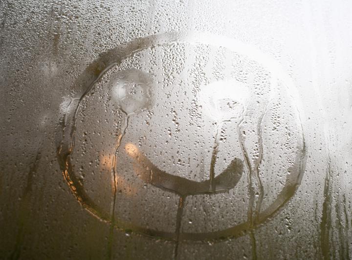 Happy smiley face emoticon hand drawn in condensation on a glass windowpane