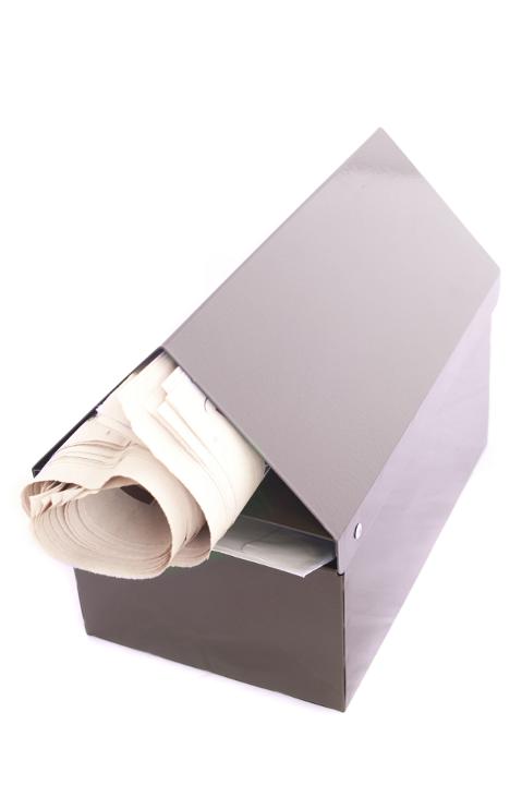 Newspaper delivery to a mail box with a rolled newspaper protruding from a plain metal letterbox isolated on white