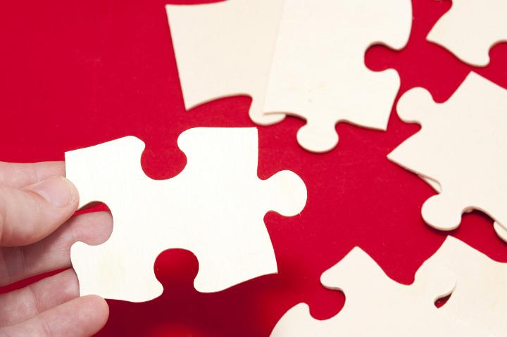 Close Up of Hand Assembling Blank Puzzle Pieces on Red Surface, Business Teamwork Concept Image