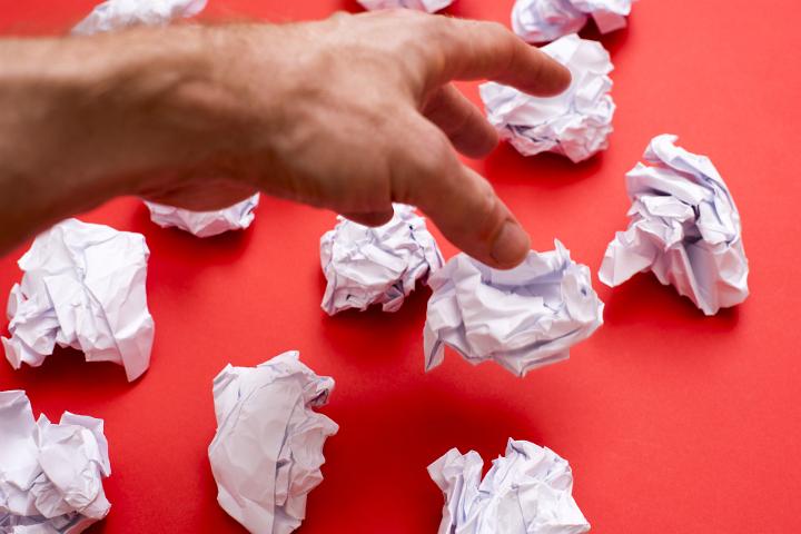 Human hand throwing away balls of paper against red background