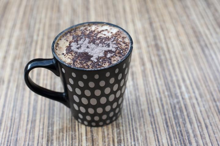 Still Life of Indulgent Cappuccino Dusted with Cocoa in Polka Dotted Mug on Table Top with Wood Grain Texture