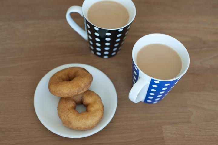 Close up Cups of Hot Coffee Drink and Tasty Doughnuts on Plate Served on Top of Wooden Table.