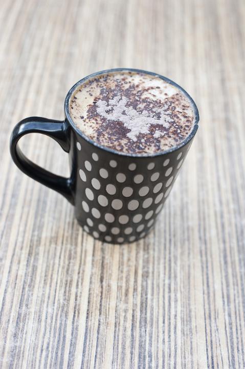 Black and white polka dot coffee mug with frothy freshly brewed coffee on a striped grey background, high angle view