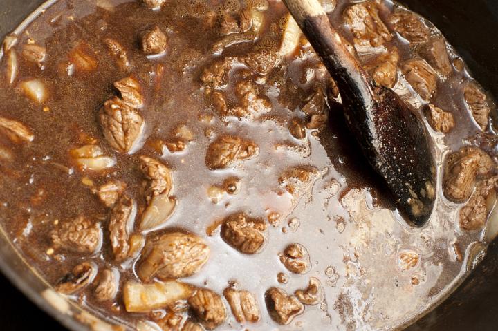 Overview of Cooking Hearty Meat Stew in Pot and Stirring with Wooden Spoon