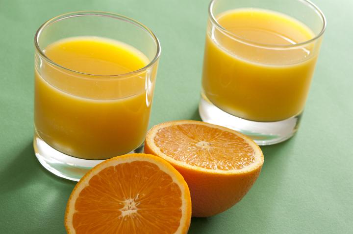 Two vibrant orange halves and glasses filled with fresh juice isolated on a plain green background.