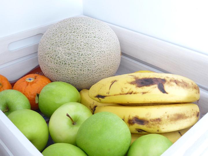 A wooden market crate filled with vibrant healthy fruits including apples, bananas, oranges and rock melon.