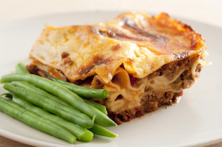 Serving of succulent meaty Italian lasagne pasta with green fresh beans, closeup view