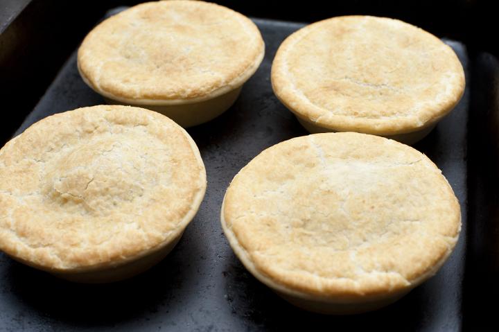 Four freshly baked meat pies topped with a golden crust in a bakery or takeaway restaurant for a quick delicious snack