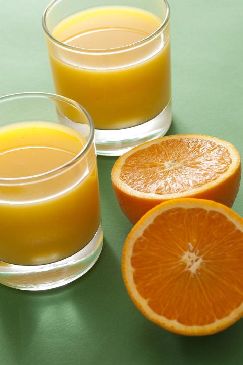 Two halves of orange fruit and glasses of juice standing on green surface