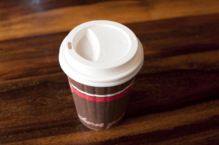 Paper takeaway coffee cup with a plastic lid for hot beverages on a wooden table, high angle view
