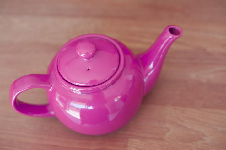 High angle view of a shiny colorful pink ceramic teapot on a wooden background with copyspace
