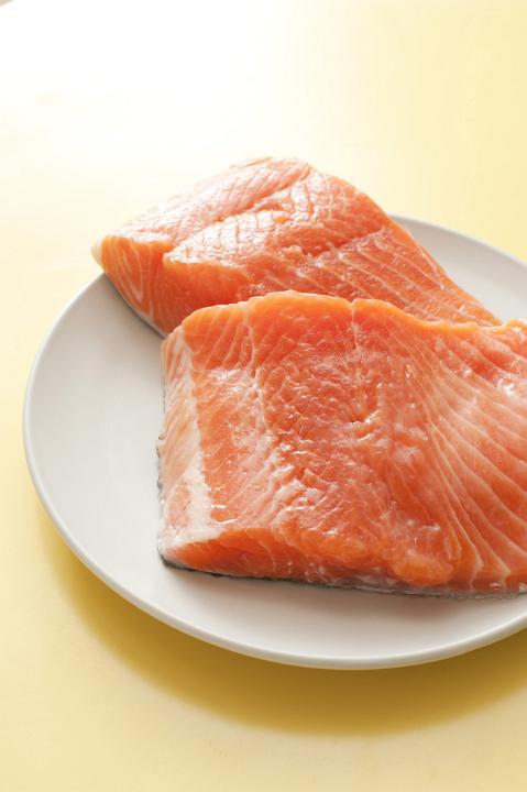 Close up Raw Salmon Fish Meat Slices on a White Plate, Placed on a Yellow Table.
