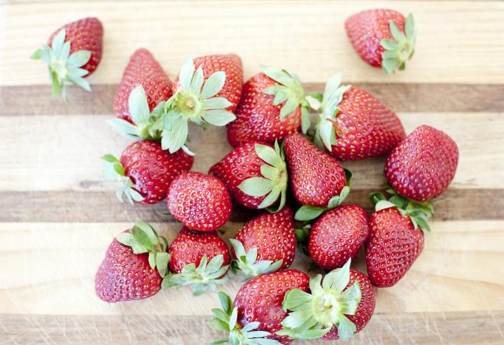 Overhead view of a pile of fresh ripe red organic strawberries harvested from the garden on a wooden board
