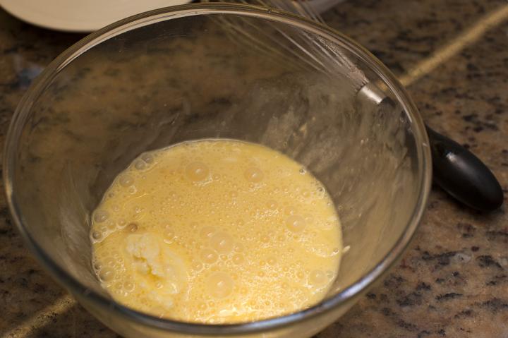 Freshly whisked eggs in a glass bowl on a wooden kitchen counter ready to be used for baking or as a cooking ingredient for breakfast