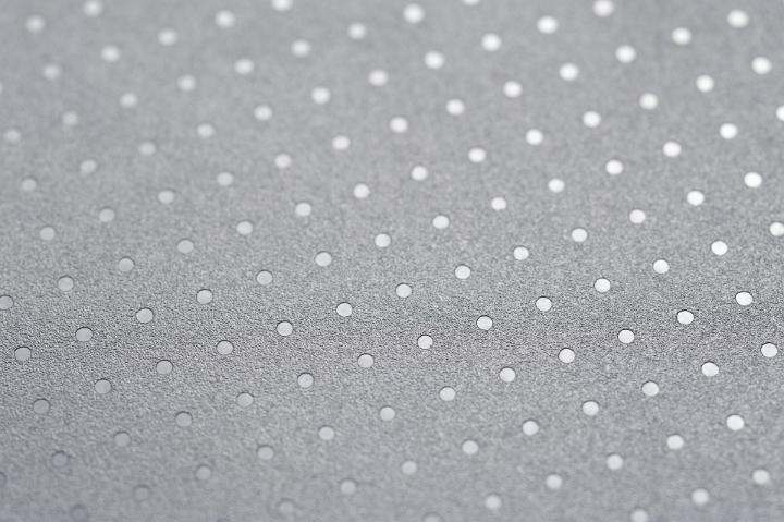 A background of oblique angled spots forming an array reflecting off a rough textured surface