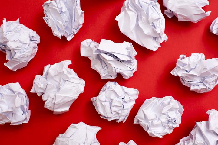 Screwed up paper rubbish, illustrating a scrapped, bad idea concept, isolated on a red background with copy space.