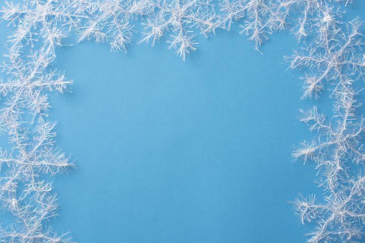 Border of white snowflake decorations on a cold toned blue winter background with copy space for your Christmas greeting