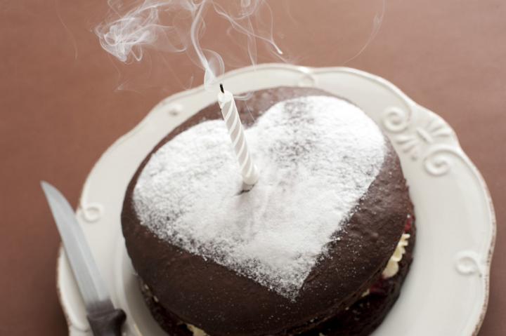 A chocolate birthday cake for a loved one with a white icing sugar heart shape on top and a single extinguished candle