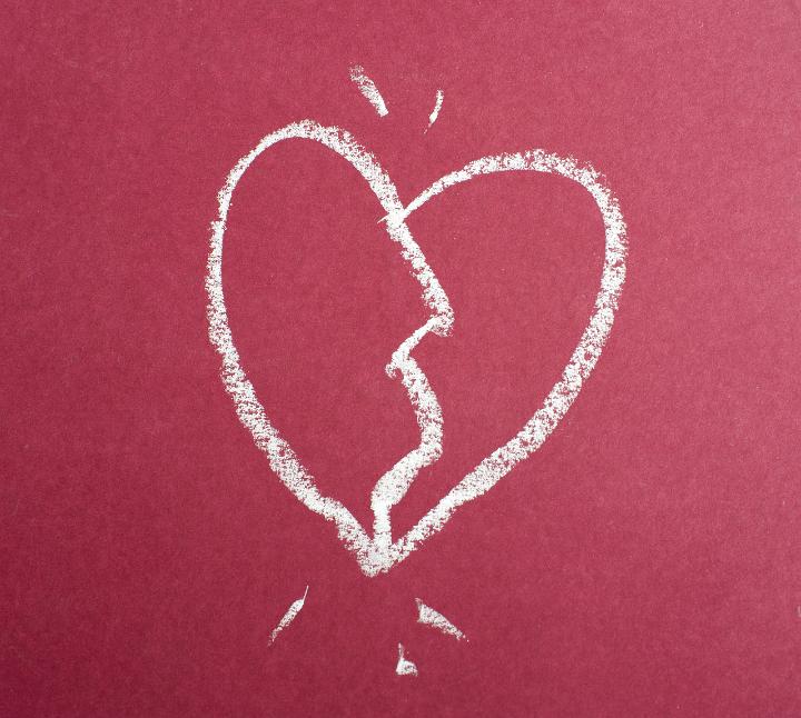 A sketched broken love heart hand drawn with white chalk on a red chalkboard.