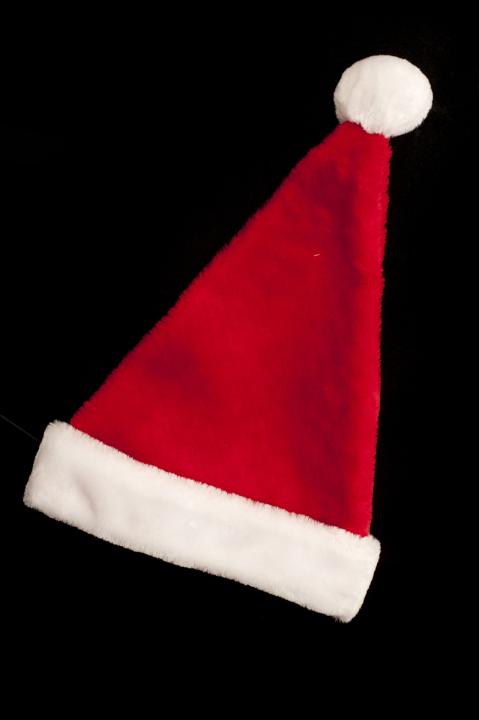 Festive red Christmas Santa hat lying diagonally on a black in vertical format for a holiday background or card