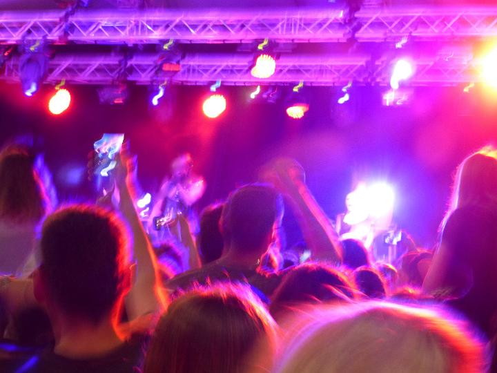 Cheering audience and fans at a concert lit by colorful pink and purple lights from the stage , view from the back