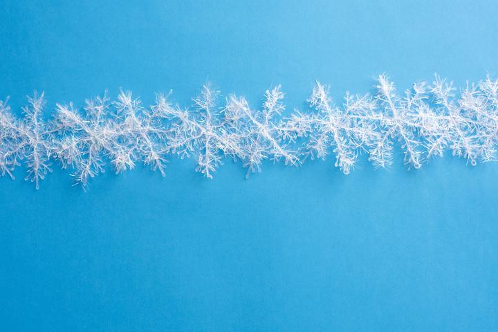 White Christmas snowflake tinsel decorations isolated on a blue background with copy space.