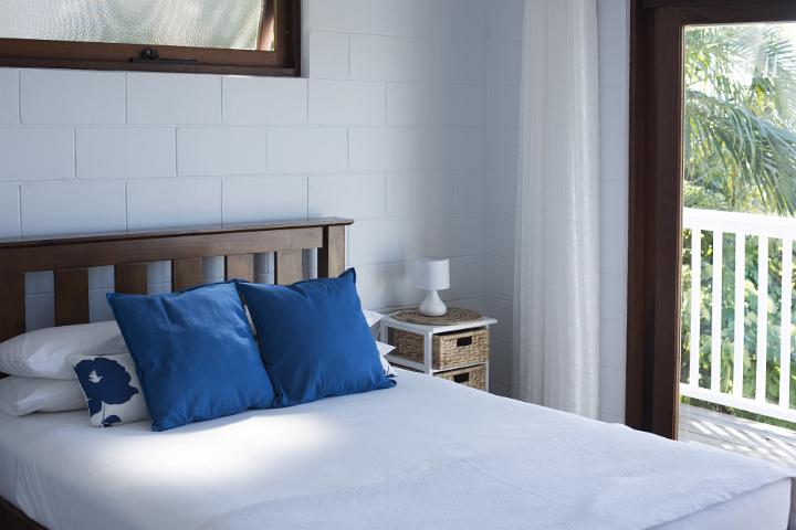A contemporary, bright white beach style bed and bedroom opening to views of tropical palm trees.