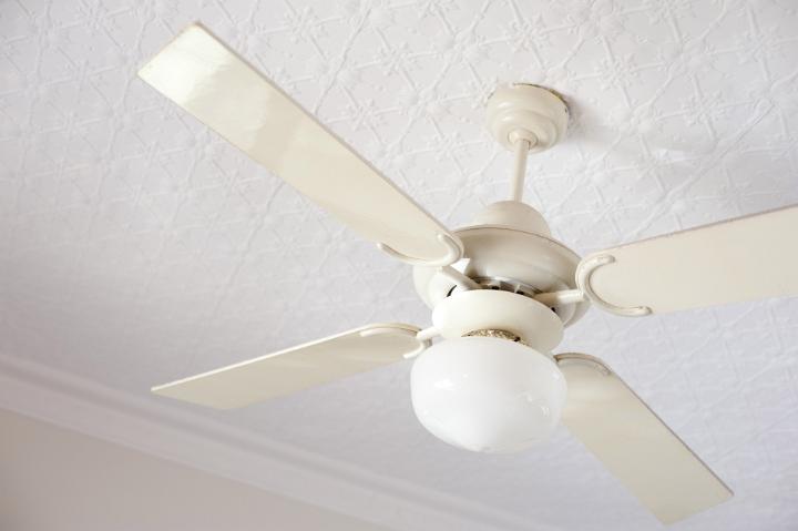 An old style, vintage ceiling fan and lamp hanging from the interior of a white home.