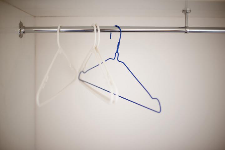 Empty wire coat hangers on a simple metal clothing rail inside a white wardrobe