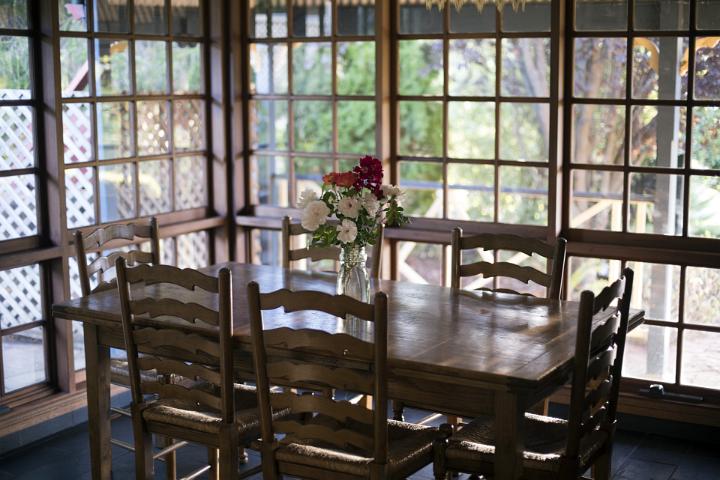 An empty, vintage timber dining room with wide windows, table and a vase of fresh flowers.