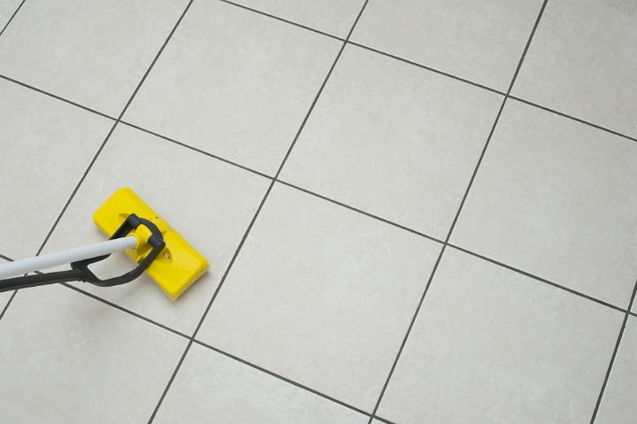 Mopping a white tiled floor using a modern yellow plastic squeegee mop in a household chores and hygiene concept