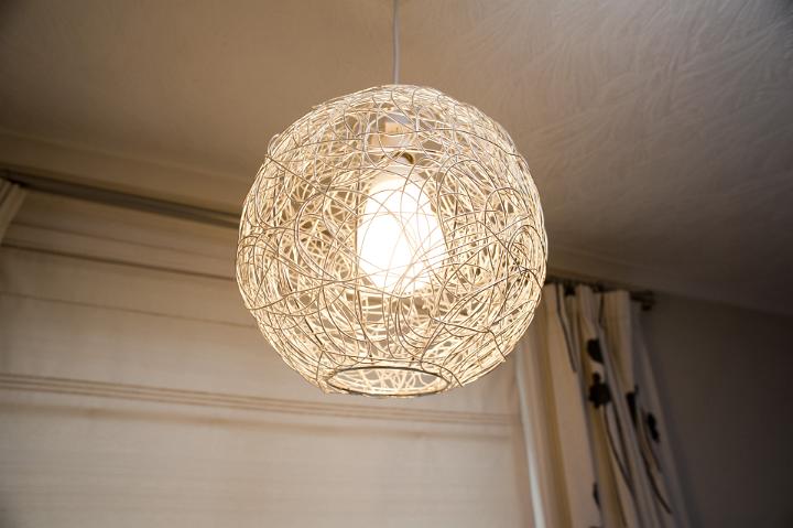 Hand crafted spherical rattan or wicker globe lampshade with an illuminated light bulb hanging from a ceiling indoors