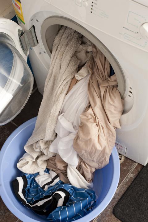 Clean washing or laundry spilling out of the front loader door a washing machine into a plastic tub in a household chores and hygiene concept