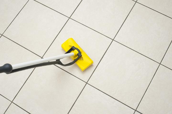 Mopping a tiled white floor with a modern squeegee plastic mop in a household hygiene concept