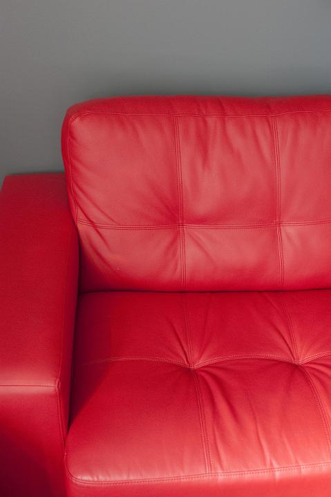 Arm and portion of a comfortable red leather upholstered settee on a grey wall, closeup detail