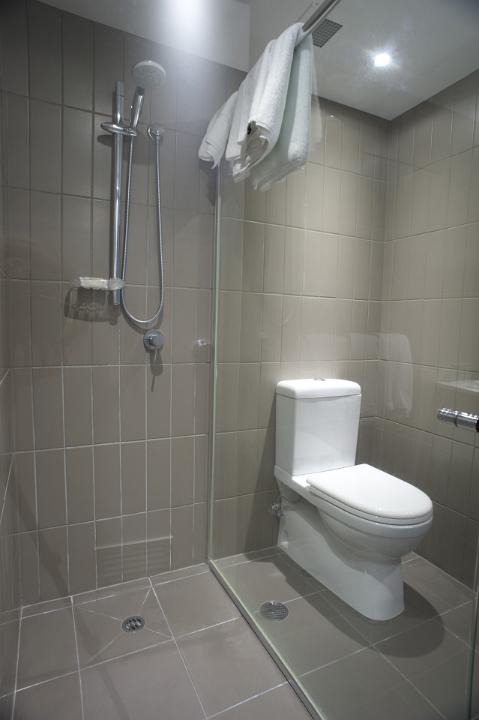 White ceramic toilet fixture and shower in a small bathroom with neutral beige decor and clean white towels