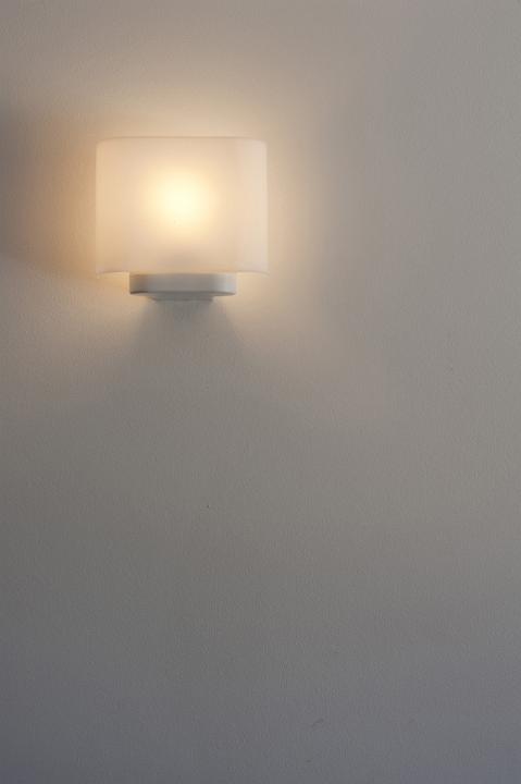 Single illuminated glowing wall sconce or wall light with a lampshade on a grey wall with copyspace