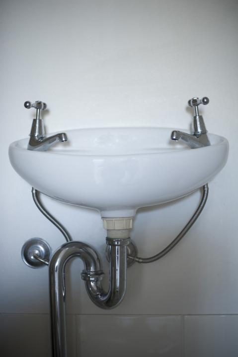 Simple ceramic white hand basin viewed low angle to show the pipes and plumbing mounted on a white wall in a restroom, or bathroom