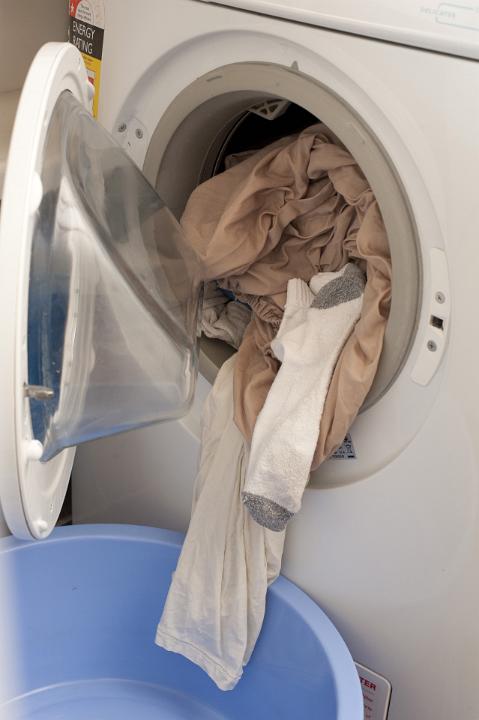 Washing spilling out of a front loader washing machine into a blue plastic basin on the floor in a cleanliness and hygiene concept