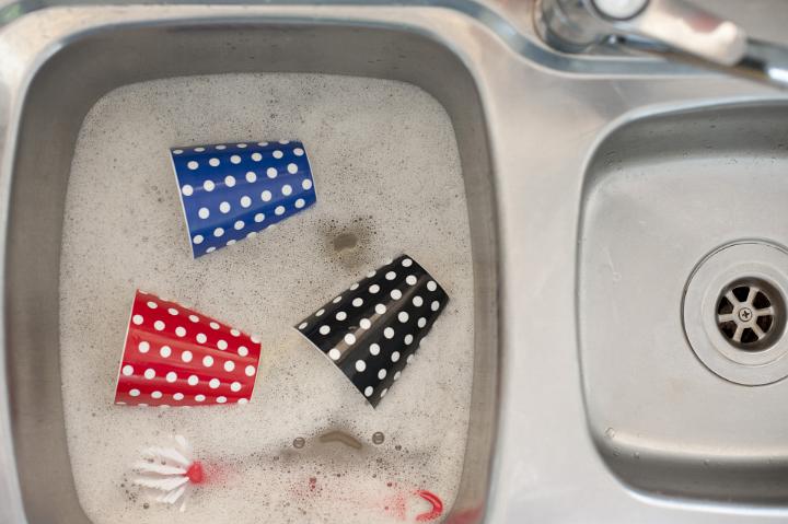 Colorful polka dot coffee mugs being washed in soapy water in a stainless steel kitchen sink, overhead view