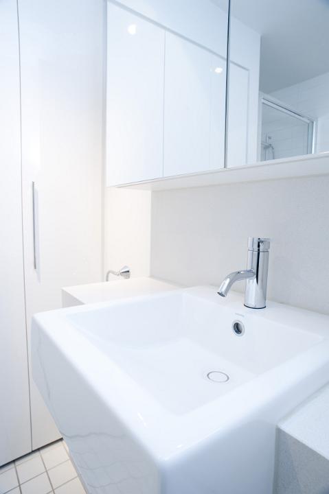 Close up interior view of a plain white handbasin and metal faucet in a white monochrome bathroom