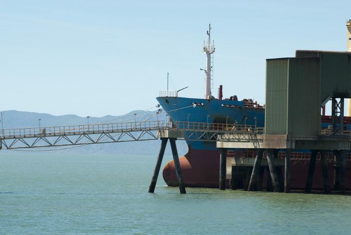 Ship docked at a wharf loading or unloading cargo at a port or harbor, view of the bows and conveyor