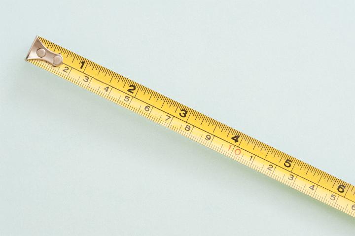 Builders retractable yellow metal tape measure with scales in inches and centimetres lying diagonally across the frame on white with copyspace