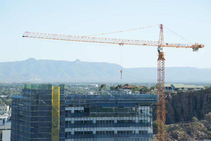 Large red industrial crane on a city skyline above a half completed commercial high-rise building in a construction and development concept